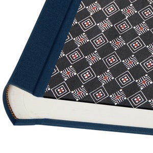May include: A hardback book with a navy blue spine and cover edges. The interior pages feature a black background with a repeating pattern of white squares and red accents. The book's pages are white.