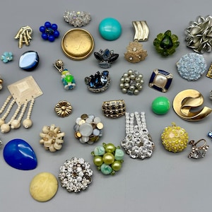 May include: A collection of vintage earrings in various colours and styles, including blue, green, white, gold, and silver. The earrings are made of different materials, such as metal, glass, and plastic. Some of the earrings are decorated with beads, rhinestones, and other embellishments.