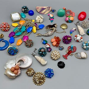 May include: A collection of colourful and whimsical earrings featuring a variety of themes, including seashells, mermaids, parrots, and lobsters. The earrings are made from a variety of materials, including metal, plastic, and beads.