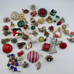 May include: A selection of vintage Christmas brooches and pins. The collection features festive designs such as a snowman, Santa Claus, Christmas trees, and other seasonal motifs in red, green, gold, and silver. Also includes earrings and a bottle stopper.