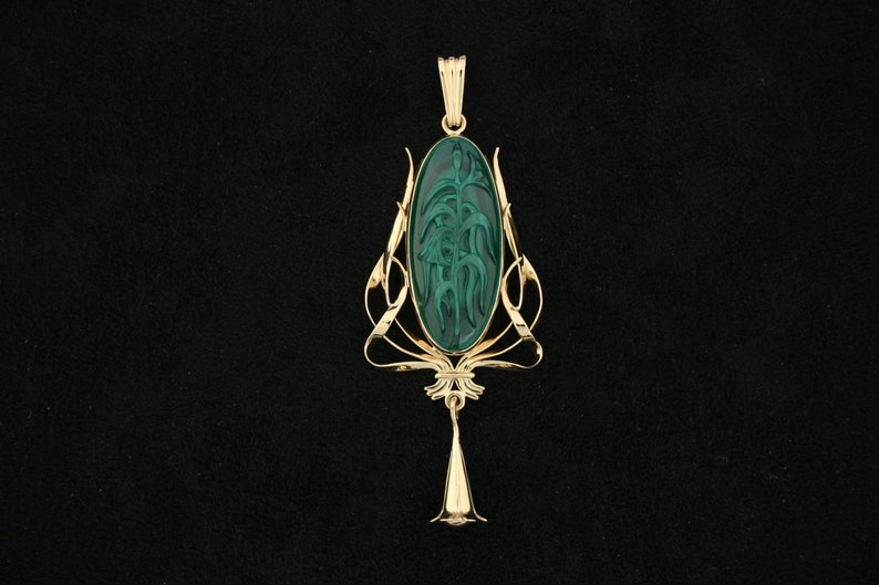 Puede incluir: Un colgante de oro con una piedra verde que presenta un dise&ntilde;o floral tallado. El colgante es de estilo Art Nouveau.