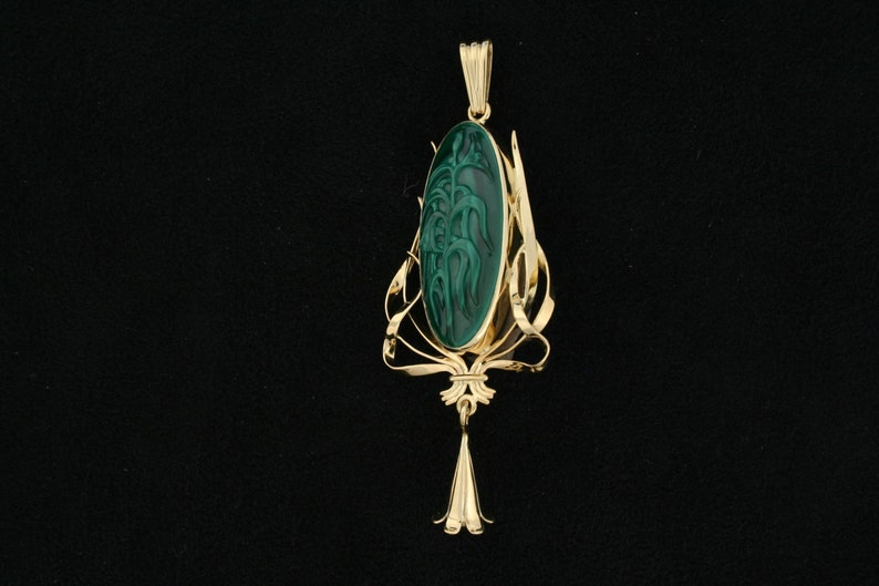 Puede incluir: Un colgante de oro con una piedra de malaquita verde tallada con un dise&ntilde;o floral. El colgante est&aacute; suspendido de una cadena delicada.