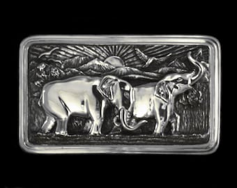 Puede incluir: Una hebilla de cinturón de plata con un diseño detallado de dos elefantes caminando por un paisaje con montañas y pájaros en el fondo.