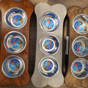 May include: Three bone-shaped wooden dog food bowls with stainless steel bowls. The bowls are in different colors: brown, gray, and brown. The bowls are labeled "Indigrow".