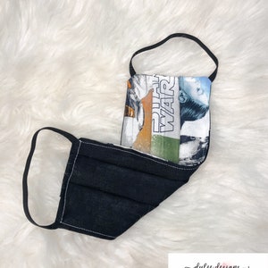 Puede incluir: M&aacute;scara facial reutilizable negra con un panel de tela con tem&aacute;tica de Star Wars que presenta el texto "Star Wars" y un personaje de la pel&iacute;cula.