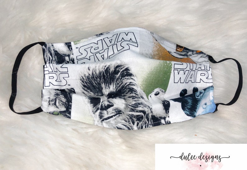 Puede incluir: Una mascarilla facial blanca con una banda el&aacute;stica negra. La mascarilla presenta un estampado de Star Wars colorido con personajes como Chewbacca y Yoda.