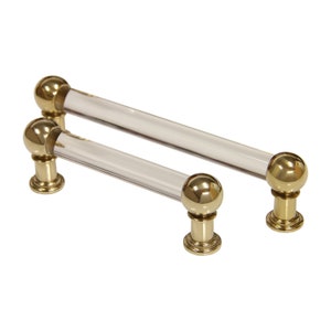 May include: Two clear glass cabinet pulls with brass knobs. The pulls are approximately 12.7 cm long.