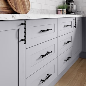 Könnte beinhalten: Hellgrauer Küchenschrank mit sechs Schubladen und schwarzen dekorativen Beschlägen. Der Schrank hat eine Marmorarbeitsplatte. Die Schubladengriffe sind schwarz und haben ein einzigartiges, strukturiertes Design.