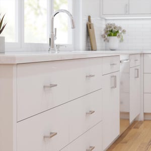 Könnte beinhalten: Moderne weiße Küche mit Edelstahlarmatur und passenden Schrankgriffen. Die Schränke haben eine glänzende Oberfläche, und die Arbeitsplatte ist hell. Ein Holzschneidebrett und eine Vase mit weißen Blumen verleihen Wärme.