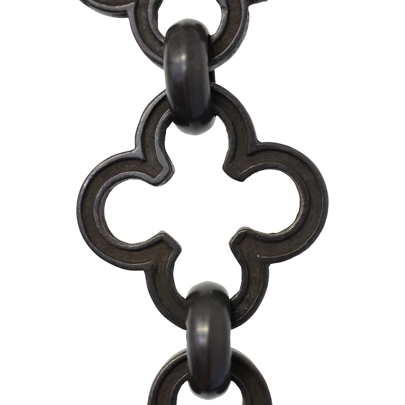 May include: Close-up of a section of a dark metal chain with a repeating quatrefoil design. The chain links are connected by oval rings. The metal has a slightly textured surface and a dark, matte finish. The background is plain white.