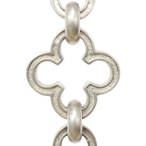 May include: Close-up of a silver-colored chain with a repeating quatrefoil design. The chain links are connected by rounded, oval-shaped connectors. The metal has a slightly textured surface, and the background is white.