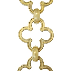 May include: Close-up of a gold-colored chain with a repeating quatrefoil design. The chain links are connected by small, rounded connectors. The background is plain white, highlighting the intricate details of the metalwork.