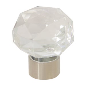 May include: A clear crystal finial with a faceted design, mounted on a silver base. The finial is a decorative element for curtains or drapery.
