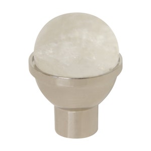 Może przedstawiać: Gałka z białego kryształu z podstawą ze srebra. Gałka jest okrągła i ma gładką powierzchnię. Podstawa jest wykonana z metalu i ma polerowane wykończenie.