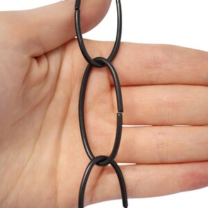 May include: Close-up of a section of a dark gray metal chain. The chain links are oval-shaped and connected. The background is a plain white surface.