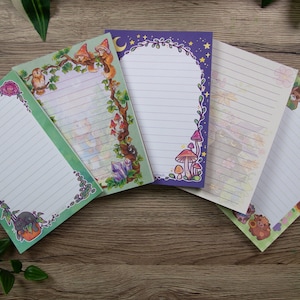Könnte beinhalten: Ein Set aus fünf rechteckigen Briefpapierbögen mit horizontalen Linien. Jeder Bogen zeigt unterschiedliche farbenfrohe Illustrationen an den Rändern, darunter Waldtiere, Pilze, Kristalle, Blumen und himmlische Muster auf weißem Hintergrund.