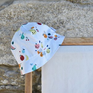 May include: White bucket hat with a colorful fruit print. The hat has a small label that says "Petit Bateau".