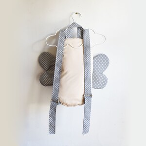 May include: A gray and white polka dot backpack with butterfly wings. The backpack has adjustable straps and a cream-colored lining.
