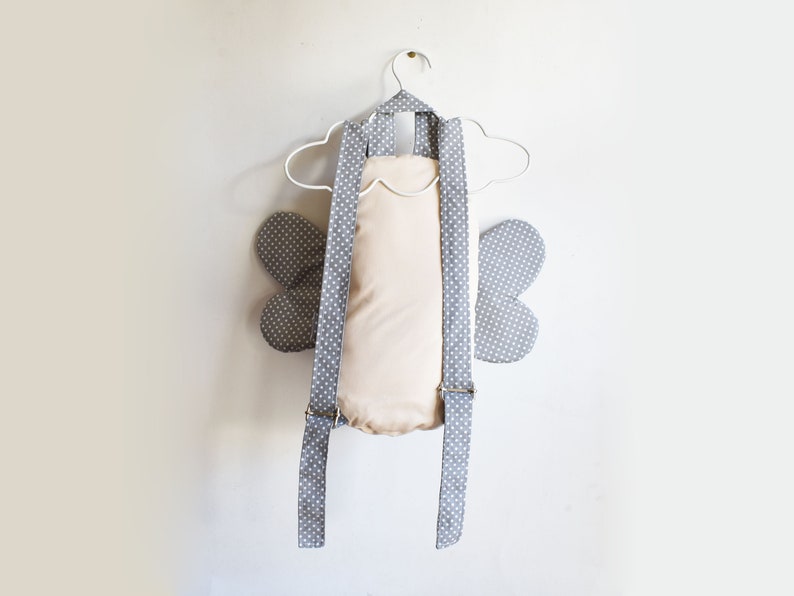 May include: A gray and white polka dot backpack with butterfly wings. The backpack has adjustable straps and a cream-colored lining.
