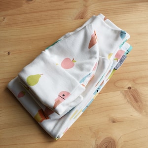 May include: A stack of white fabric baby clothes with a colorful fruit and ice cream print. The fabric is soft and comfortable for babies.