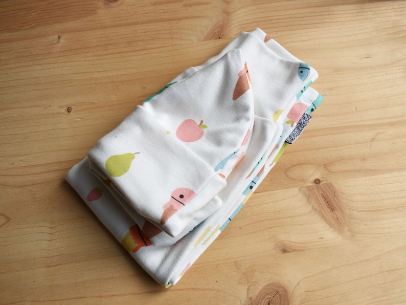 May include: A stack of white fabric baby clothes with a colorful fruit and ice cream print. The fabric is soft and comfortable for babies.