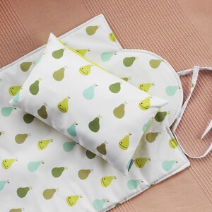 May include: A white baby bedding set with a pear pattern in shades of green, yellow, and blue. The set includes a rectangular pillow, a changing pad, and a round pad with ties. The pillow has a yellow trim.