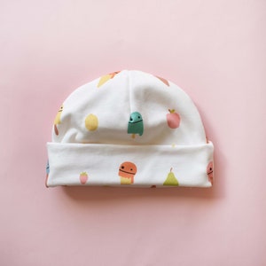 May include: White baby hat with a colorful pattern of ice cream cones, fruit, and strawberries.