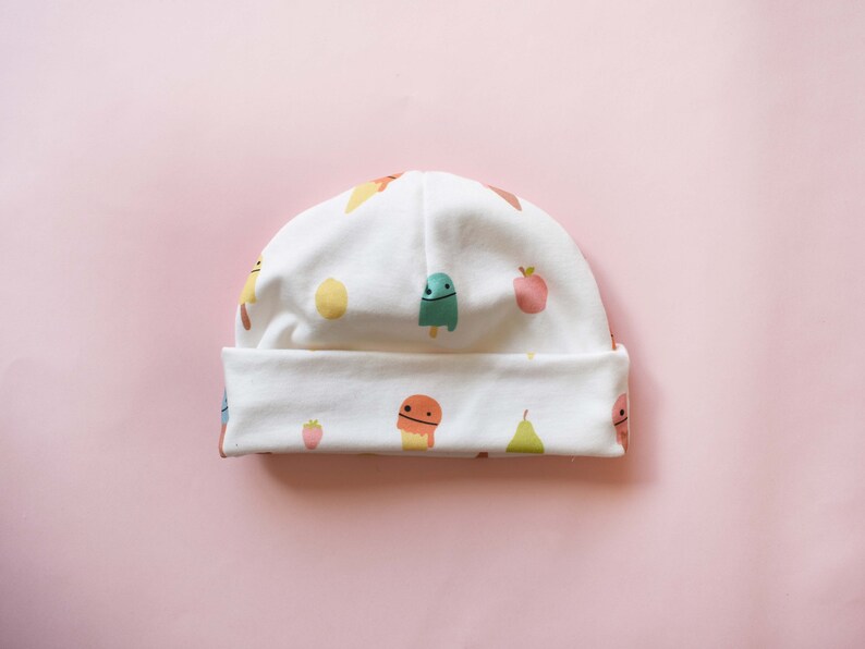 May include: White baby hat with a colorful pattern of ice cream cones, fruit, and strawberries.