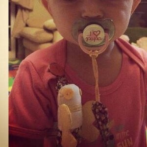 Puede incluir: Un ni&ntilde;o peque&ntilde;o con una camisa rosa con un chupete sujeto a un juguete. El chupete tiene un dise&ntilde;o rosa y blanco con el texto "I love papa" en &eacute;l. El juguete es un b&uacute;ho de peluche con un ojo de bot&oacute;n.