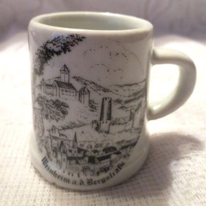 May include: White ceramic mug with a black and white illustration of a castle and town. The text "Weinheim a.d. Bergstrasse" is printed on the bottom of the mug.