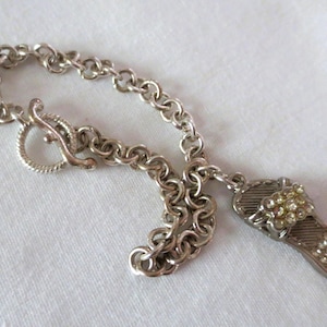 May include: Silver-toned bracelet with a toggle clasp and a charm shaped like a sandal. The sandal charm is embellished with small, clear rhinestones. The bracelet is made of a chain link design.