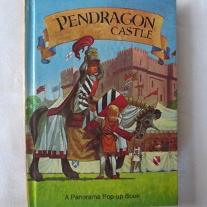 May include: A children's book titled "Pendragon Castle" with a colorful illustration of a knight on horseback. The cover features a castle scene with flags and the text "A Panorama Pop-up Book". The book has a blue sky background.