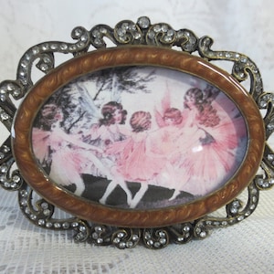 May include: An oval-shaped picture frame with a brown and gold finish. The frame is decorated with rhinestones and features a picture of a group of fairies in pink dresses.