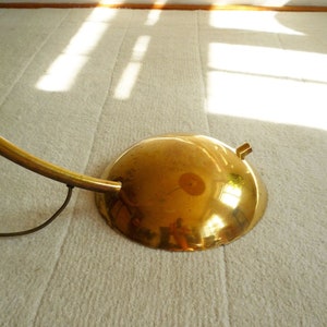 May include: A gold-toned floor lamp with a curved arm and a round, reflective base. The lamp is on a white carpet.