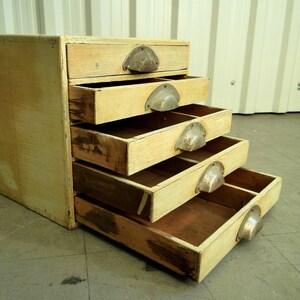 May include: A vintage wooden cabinet with six drawers. The drawers are painted a light yellow color and have metal handles. The cabinet is sitting on a gray concrete floor.