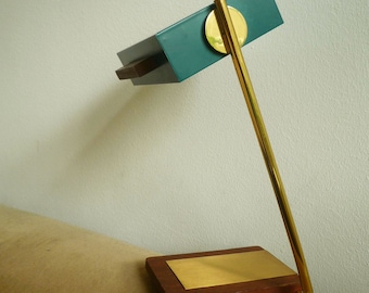 May include: A teal blue desk lamp with a brass arm and a wooden base. The lamp has a round brass accent on the top.