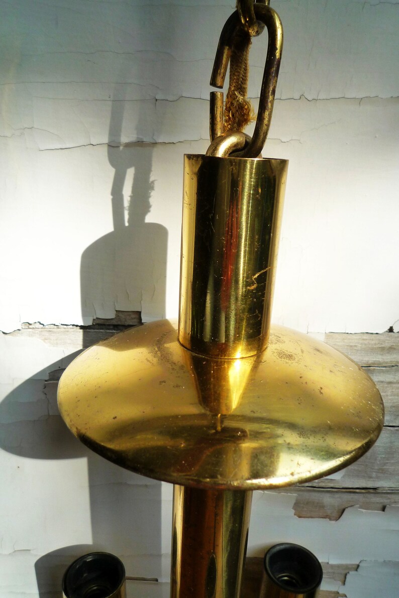 Puede incluir: Una l&aacute;mpara de ara&ntilde;a de metal dorado con una cadena y una parte superior redonda y plana. La l&aacute;mpara de ara&ntilde;a tiene tres accesorios de luz.