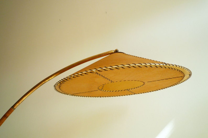 May include: A gold-toned floor lamp with a curved arm and a large, round, tan-colored lampshade with a stitched edge.
