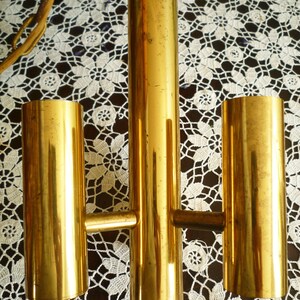 Puede incluir: Una l&aacute;mpara de ara&ntilde;a de metal dorado con tres luces. La l&aacute;mpara tiene un dise&ntilde;o sencillo con tres luces cil&iacute;ndricas unidas a una varilla central.