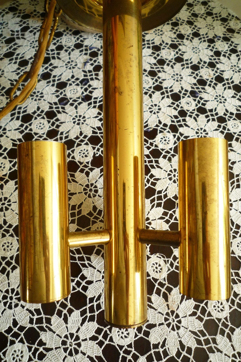 Puede incluir: Una l&aacute;mpara de ara&ntilde;a de metal dorado con tres luces. La l&aacute;mpara tiene un dise&ntilde;o sencillo con tres luces cil&iacute;ndricas unidas a una varilla central.