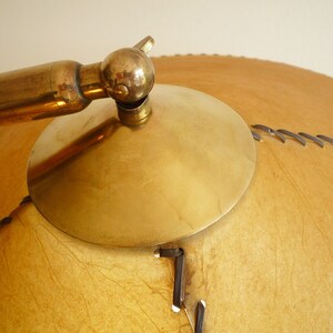May include: A brass lamp with a large, round, tan leather shade. The shade has a stitched design and a brass trim.