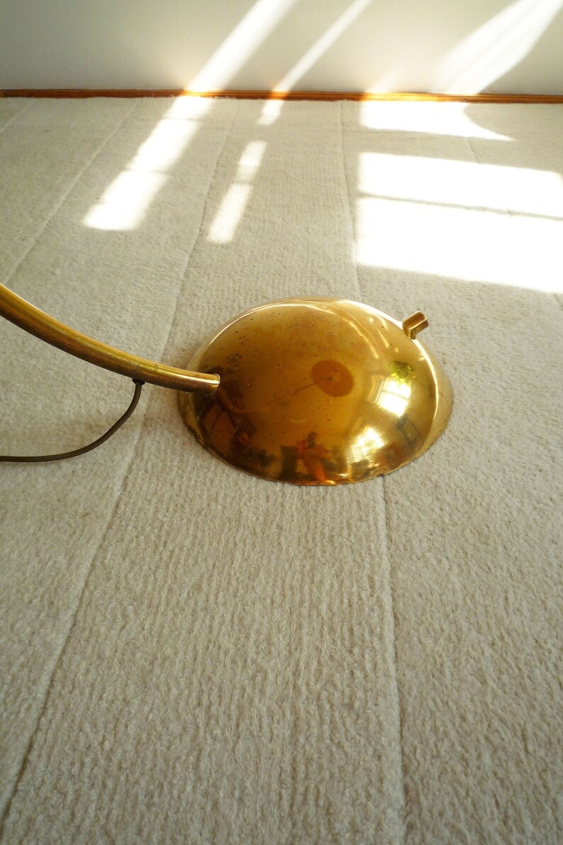 May include: A gold-toned floor lamp with a curved arm and a round, reflective base. The lamp is on a white carpet.