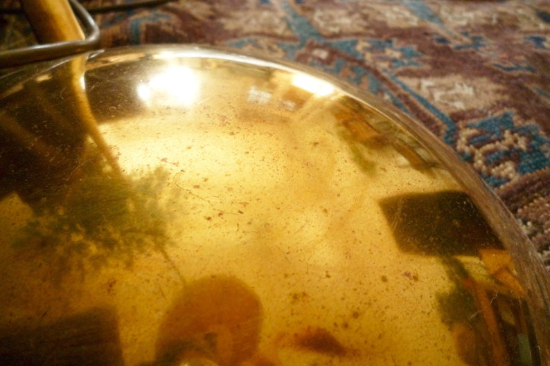 May include: A close-up of a gold-colored metal lampshade with a textured surface. The lampshade is reflecting light and has a warm, golden hue.