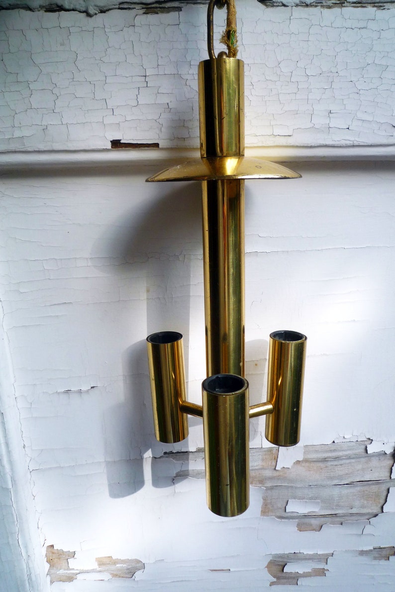 Puede incluir: Una l&aacute;mpara de ara&ntilde;a de metal dorado con tres luces. La l&aacute;mpara tiene una c&uacute;pula circular y un tallo largo y cil&iacute;ndrico.