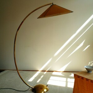 May include: A gold floor lamp with a curved arm and a brown, circular lampshade. The lamp is on a white rug in a room with a wooden table.