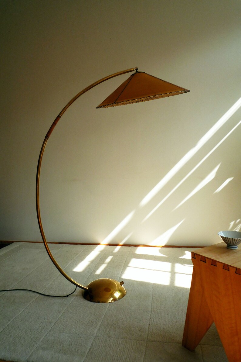 May include: A gold floor lamp with a curved arm and a brown, circular lampshade. The lamp is on a white rug in a room with a wooden table.