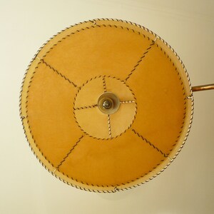 May include: A round, tan lampshade with a stitched design and a metal arm.
