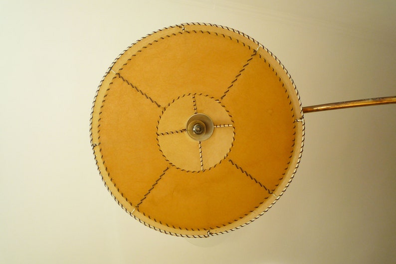 May include: A round, tan lampshade with a stitched design and a metal arm.