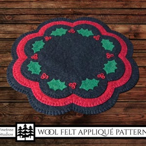 May include: Wool felt applique pattern for a Christmas wreath with red and green holly leaves and berries. The pattern is on a dark blue background with a red border.