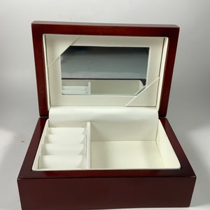 May include: A dark wood jewelry box with a white interior and a mirror inside the lid. The box has a compartment for rings and a larger compartment for other jewelry.
